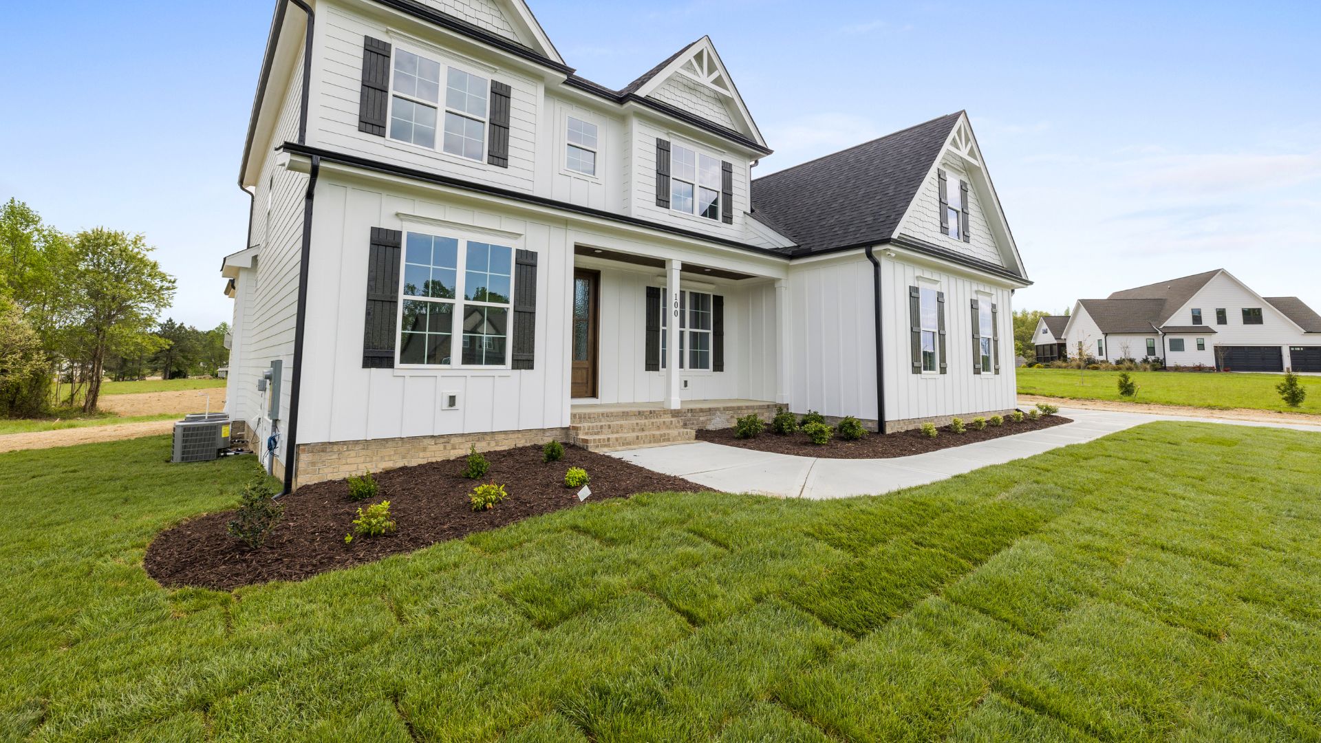 White two-story house with black shutters and manicured lawn in suburban setting