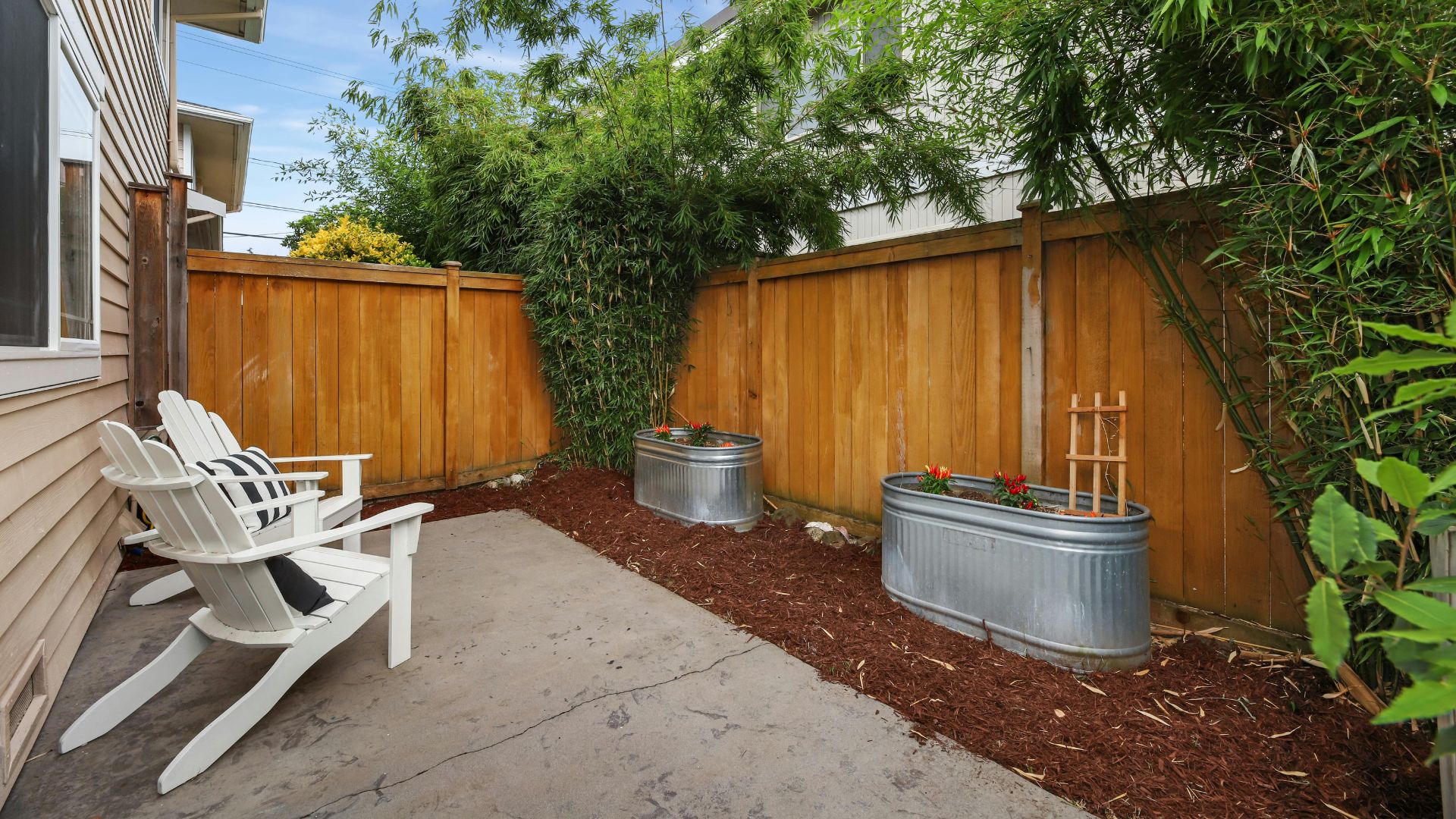 Backyard patio with white Adirondack chairs, metal planters, and wooden fence