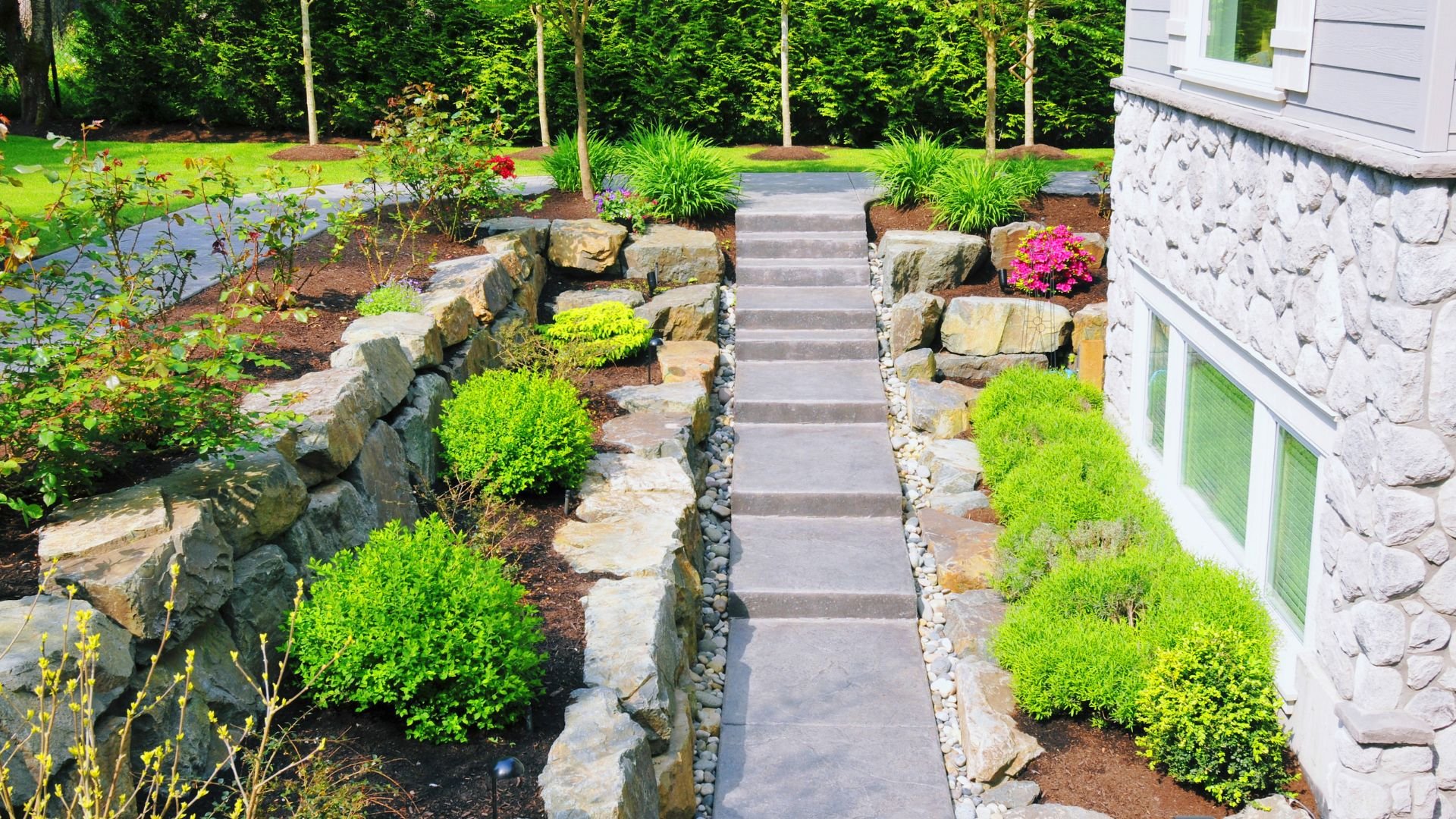 Stone steps with green shrubs and rock walls leading to a white house